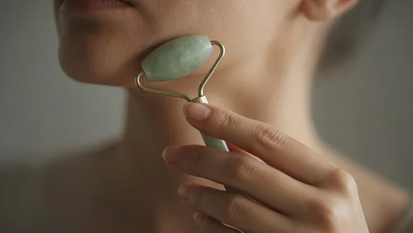 A hand holding a jade roller, rolling lightly along the jawline toward the ear
